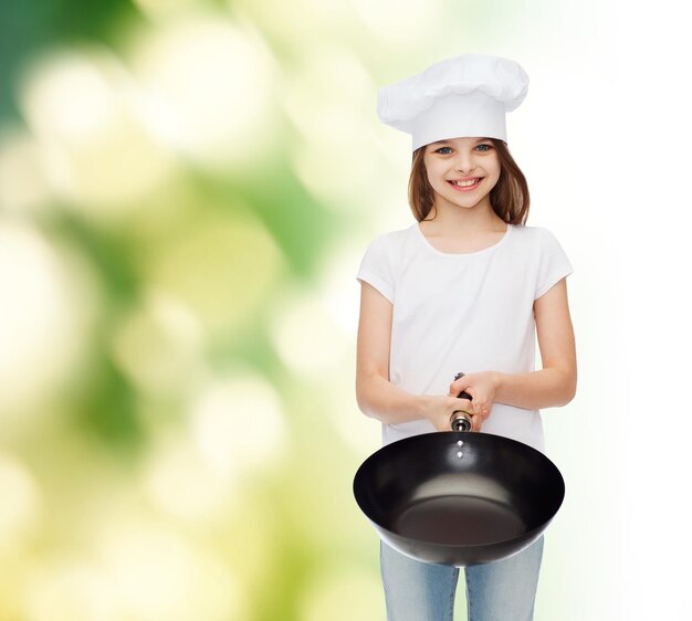 advertising, childhood, cooking and people - smiling girl in white t-shirt and cooking hat holding pan over green background