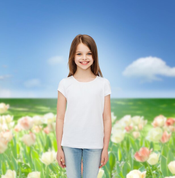 advertising, childhood, nature and people concept - smiling little girl in white blank t-shirt over flower field background