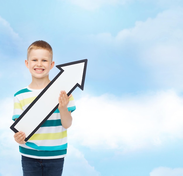 advertising, direction and childhood concept - smiling little boy with white blank arrow pointing up over cloudy sky background