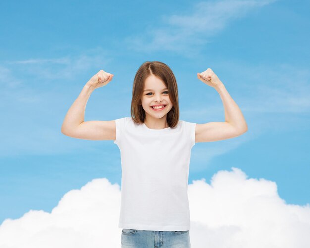 advertising, dream, childhood, gesture and people - smiling little girl in white blank t-shirt with raised arms over blue sky background