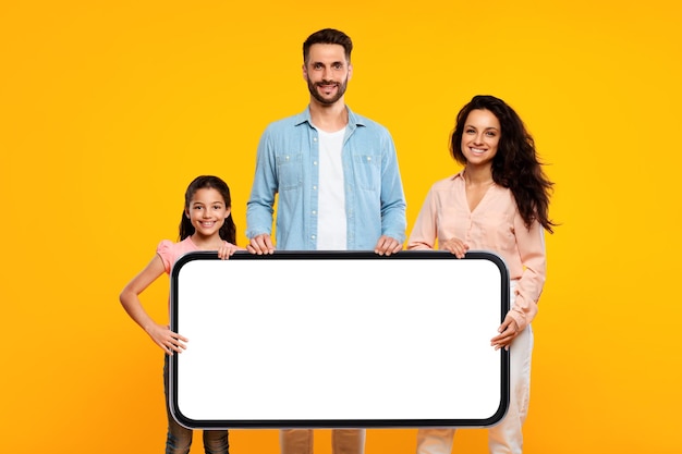 Advertising european family of three holding big horizontal smartphone with white blank screen