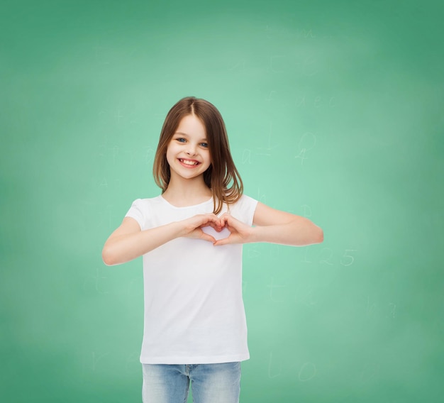 advertising, gesture, charity, education and people - smiling little girl in white blank t-shirt over green board background
