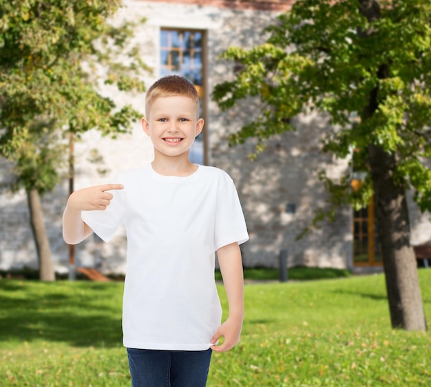 advertising, gesture, people and childhood concept - smiling boy in white blank t-shirt pointing finger at himself over campus background