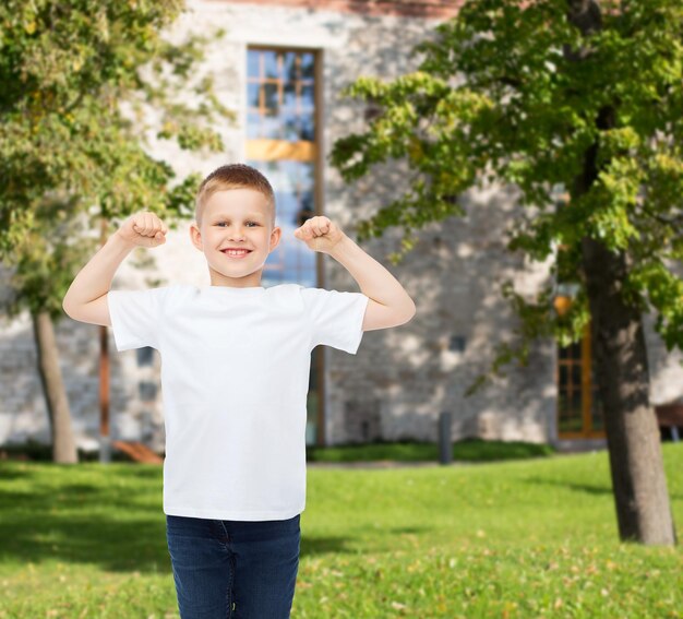 advertising, gesture, people and childhood concept - smiling little boy in white blank t-shirt with raised hands over campus background