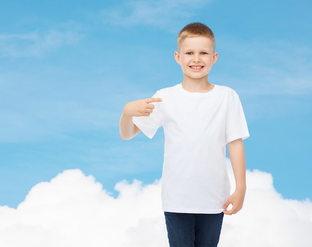 advertising, gesture, people and childhood concept - smiling little boy in white t-shirt pointing finger at himself over sky background