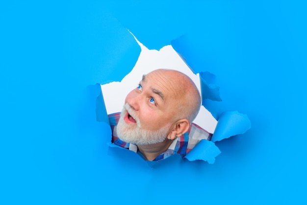 Advertising man through hole in blue paper surprised bearded man making hole in paper attractive man