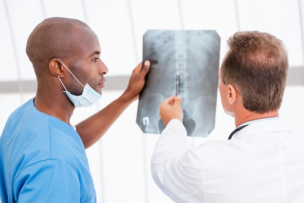 Advisering over röntgen. Twee zelfverzekerde artsen die röntgenfoto's onderzoeken terwijl een van hen erop wijst
