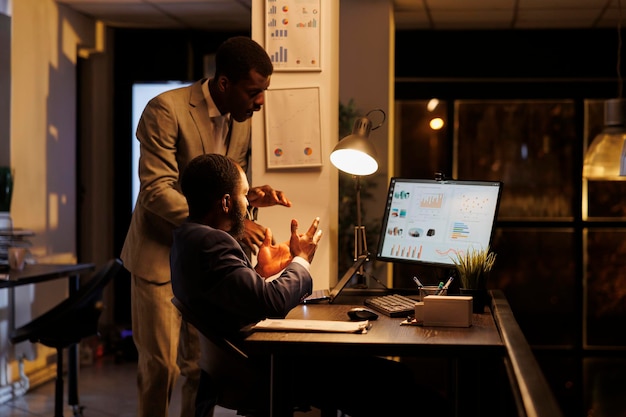 Advisor agent showing financial statistics to worker, discussing marketing strategy in startup office. Corporate employees working overhours at company investment planning profit plan