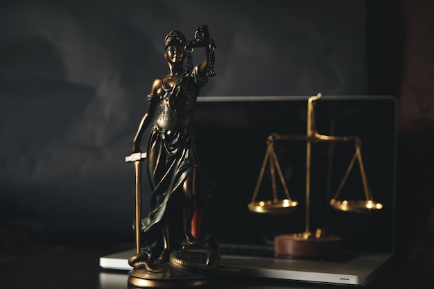 Advocaten kantoor. Standbeeld van Justitie met schalen en advocaat die op een laptop werkt. Juridisch recht, advies en rechtvaardigheidsconcept.