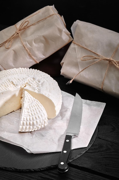 삼각형 모양의 조각으로 잘라진 아디게 치즈 인근에는 나무로 된 종이에 포장 된 세 개의 치즈 머리가 있습니다.