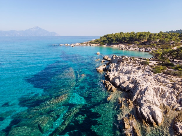 Costa del mar egeo con acqua blu trasparente, vegetazione intorno, rocce, cespugli e alberi, vista dal fuco, montagna grecia