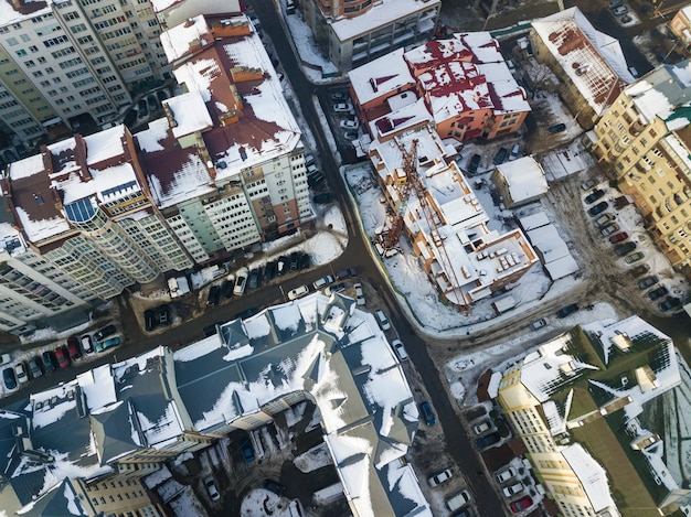 Aerial black and white winter top view of modern city center with tall buildings and parked cars on snowy streets.