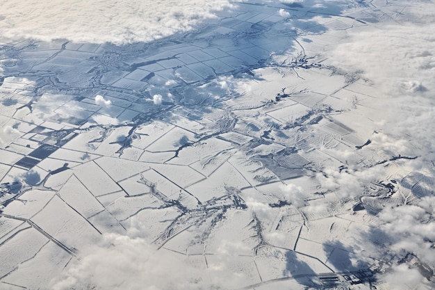 Aerial cloudscape view over clouds top to snow covered rivers roads cities and fields winter air