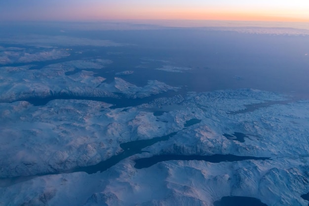 Aerial dramatic top view on snow covered mountains and glaciers in Greenland coastal area