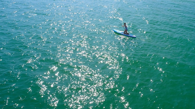 Aerial drone birds eye view of young woman exercising sup board in turquoise tropical clear waters