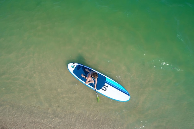 Aerial drone birds eye view of young woman exercising sup board in turquoise tropical clear waters