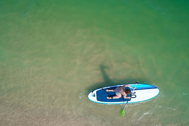 Aerial drone birds eye view of young woman exercising sup board in turquoise tropical clear waters