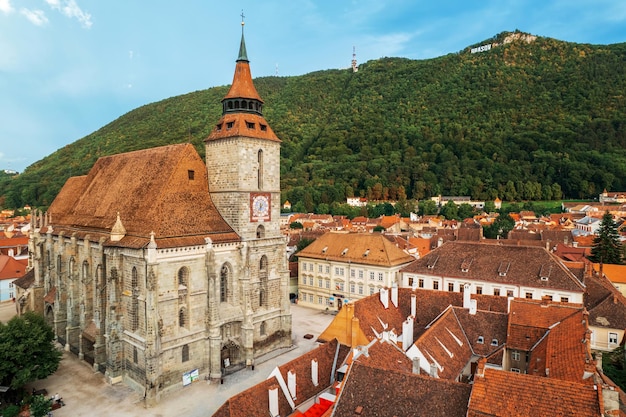 Foto vista aerea del drone della chiesa nera nel vecchio centro di brasov, romania vecchi edifici residenziali intorno ad essa colline con verde