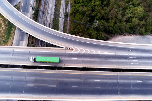 Aerial drone view of cargo white truck on highway road with\
green container, transportation concept,import,export logistic\
industrial transporting land transport on the asphalt\
expressway