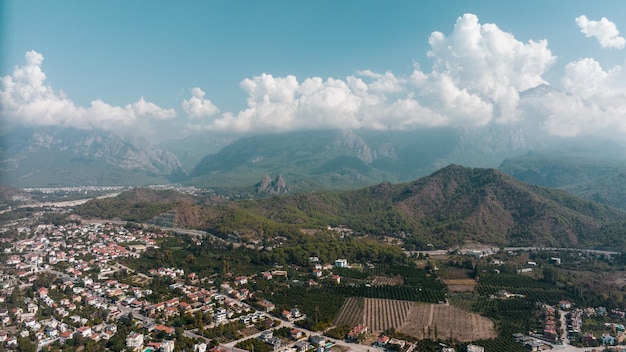 Aerial drone view of the city at the foot of the green mountains Clear sunny day White clouds Green hills