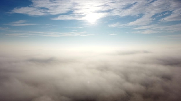 Aerial drone view flight over fog and under clouds with shining sun shining