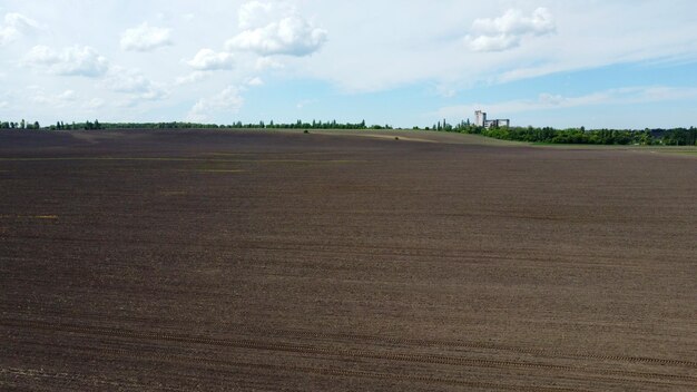 Aerial drone view flight over huge plowed field and blue sky skyline horizon black earth agriculture