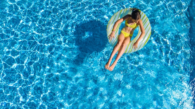 Aerial drone view of little girl in swimming pool from above, kid swims on inflatable ring donut , child has fun in blue water on family vacation resort