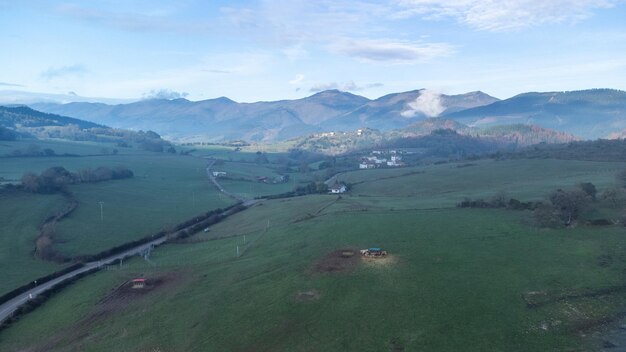 Aerial drone view of mountain road and green meadows on cloudy day with fog