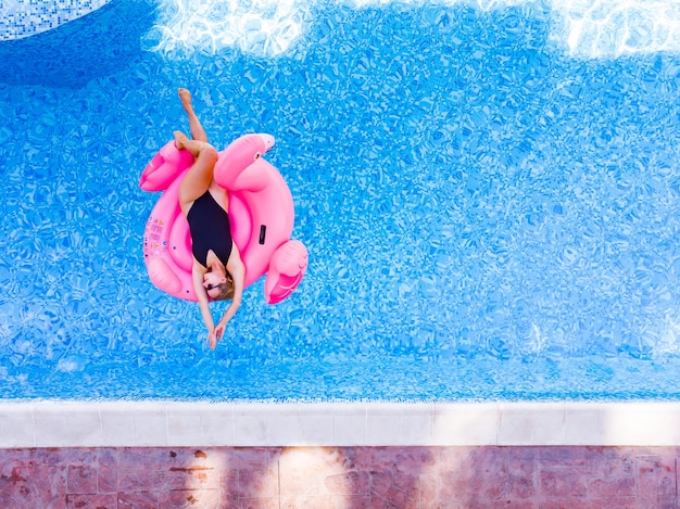 Aerial drone view of woman on flamingo pool float in pool