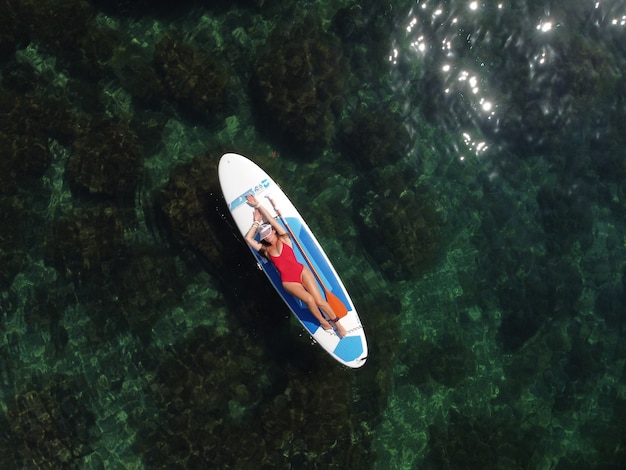 Photo aerial drone view on young attractive brunette woman with long hair in red swimsuit swimming on sup