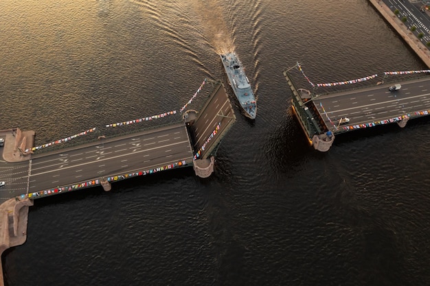 写真 隆起した宮殿跳ね橋の上面図の黒い水の色の下で軍艦の空中風景が通過します...