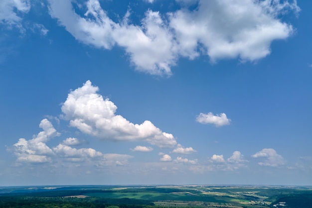 明るい夏の日に作物が育ち、遠くの森がある緑の耕作された農地の上の澄んだ青い空の空中風景ビュー