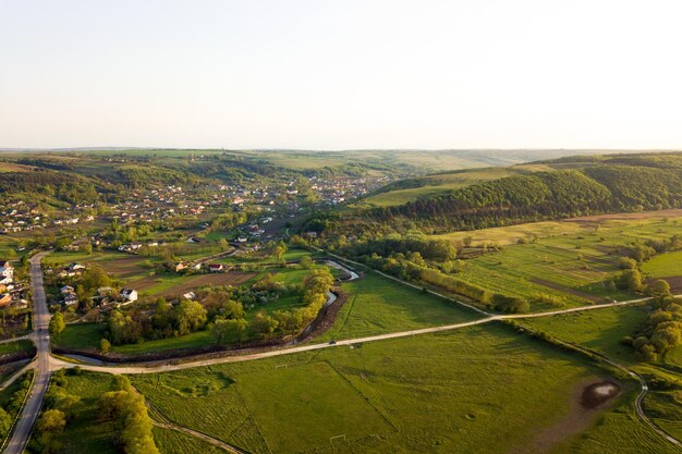 Вид с воздуха на зеленые возделываемые сельскохозяйственные поля с растущими культурами и отдаленными деревенскими домами в яркое лето