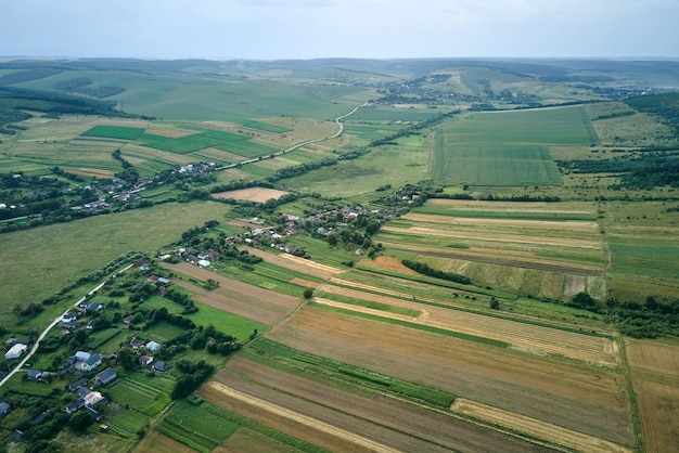 Aerial landscape view of green cultivated agricultural fields with growing crops and distant village houses