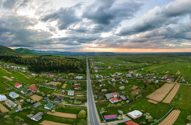 Aerial landscape view of village houses and distant green cultivated agricultural fields with growing crops on bright summer day