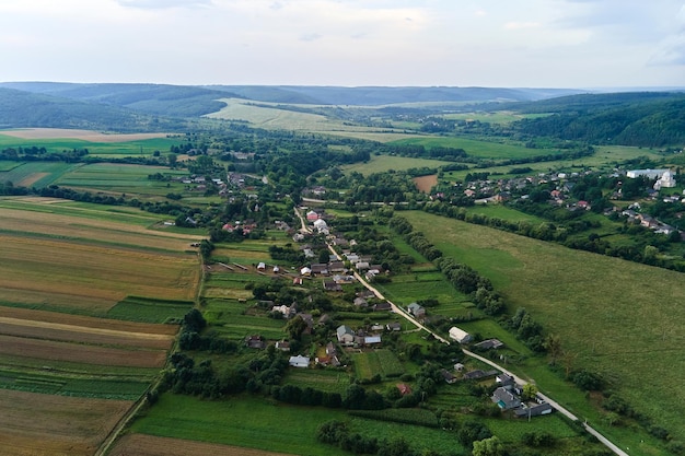 Aerial landscape view of village houses and distant green cultivated agricultural fields with growing crops on bright summer day