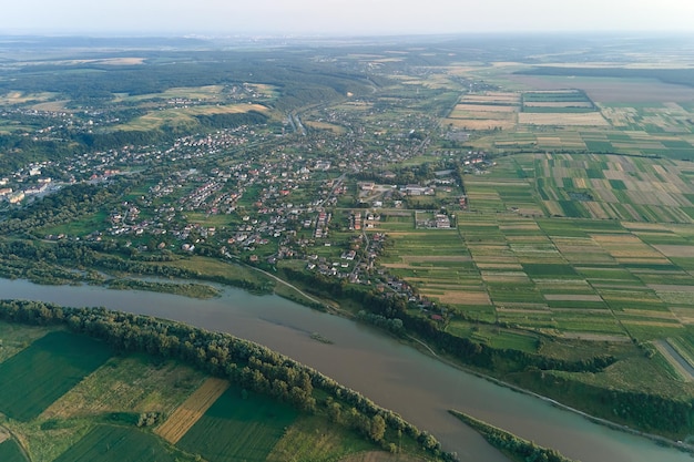 Aerial landscape view of village houses and distant green cultivated agricultural fields with growing crops on bright summer day