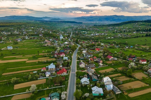 Aerial landscape view of village houses and distant green cultivated agricultural fields with growing crops on bright summer day