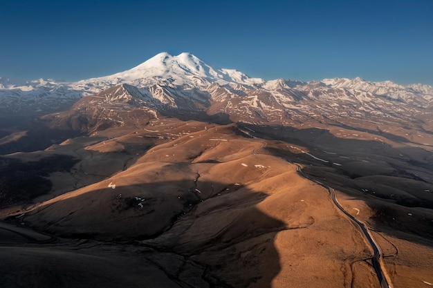 Aerial landscape with road going along hilltops to snowcovered high mountain MtElbrus Russia