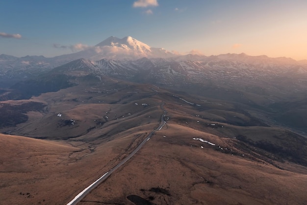 Aerial landscape with road going along hilltops to snowcovered high mountain MtElbrus Russia