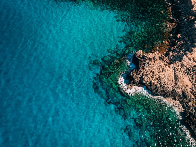 Aerial overhead Rocky seashore with crystal clear blue water near Cape Cavo Greco, Cyprus