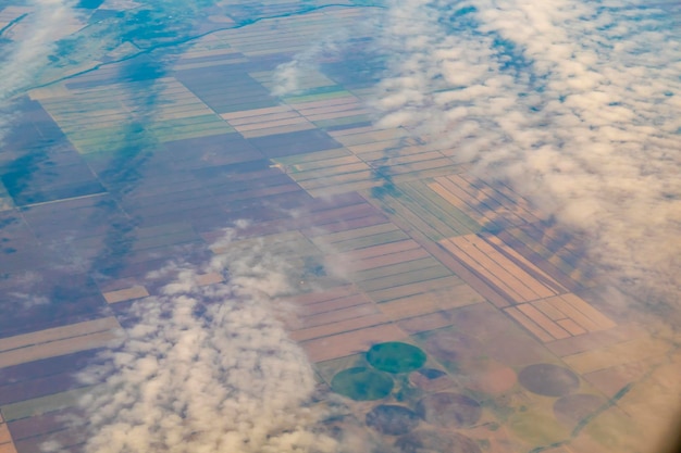 Aerial photo of farmland view from the plane to the ground\
squares of fields under the clouds