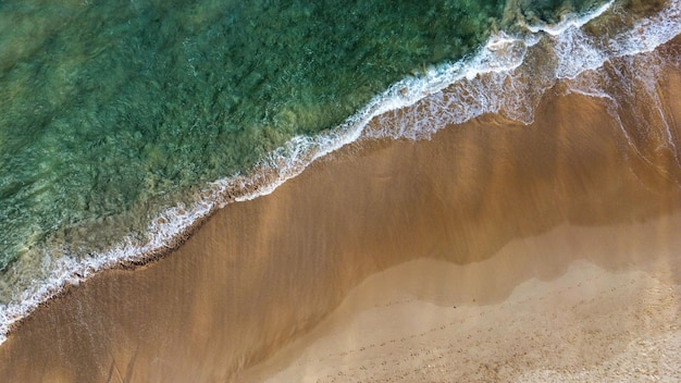 Aerial shot of a beautiful green colored sea's foamy waves hitting the seashore