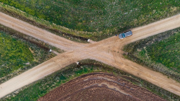 Aerial shot of a car at a crossroad in the middle of a fiel