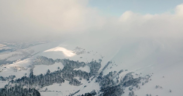 Aerial shot of majestic sunrise in the mountains Valley between the mountains is covered with fog and is illuminated by the warm rays of the rising sun Mountains covered with forest natural