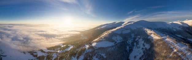 Aerial shot of majestic sunrise in the mountains Valley between the mountains is covered with fog and is illuminated by the warm rays of the rising sun Mountains covered with forest natural