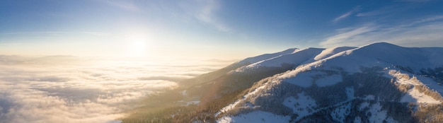 Aerial shot of majestic sunrise in the mountains Valley between the mountains is covered with fog and is illuminated by the warm rays of the rising sun Mountains covered with forest natural