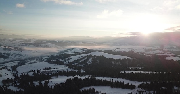 Aerial shot of majestic sunrise in the mountains valley between\
the mountains is covered with fog and is illuminated by the warm\
rays of the rising sun mountains covered with forest natural