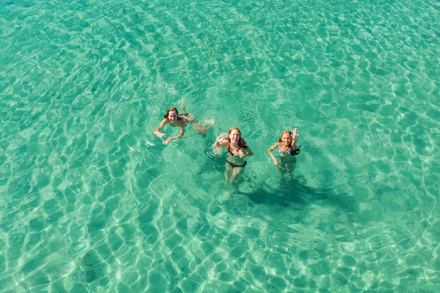 Ripresa aerea di tre belle giovani amiche vestite con un bikini che si diverte tra le onde del mare limpido.