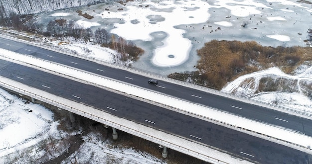 Aerial snowy bridge winter road white frozen lakes and asphalted track traffic icy river water in